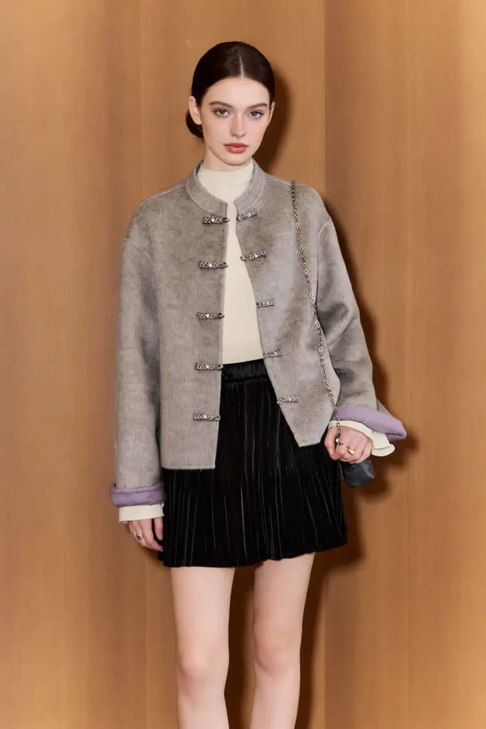 Woman wearing a gray textured jacket with silver buttons against a beige background