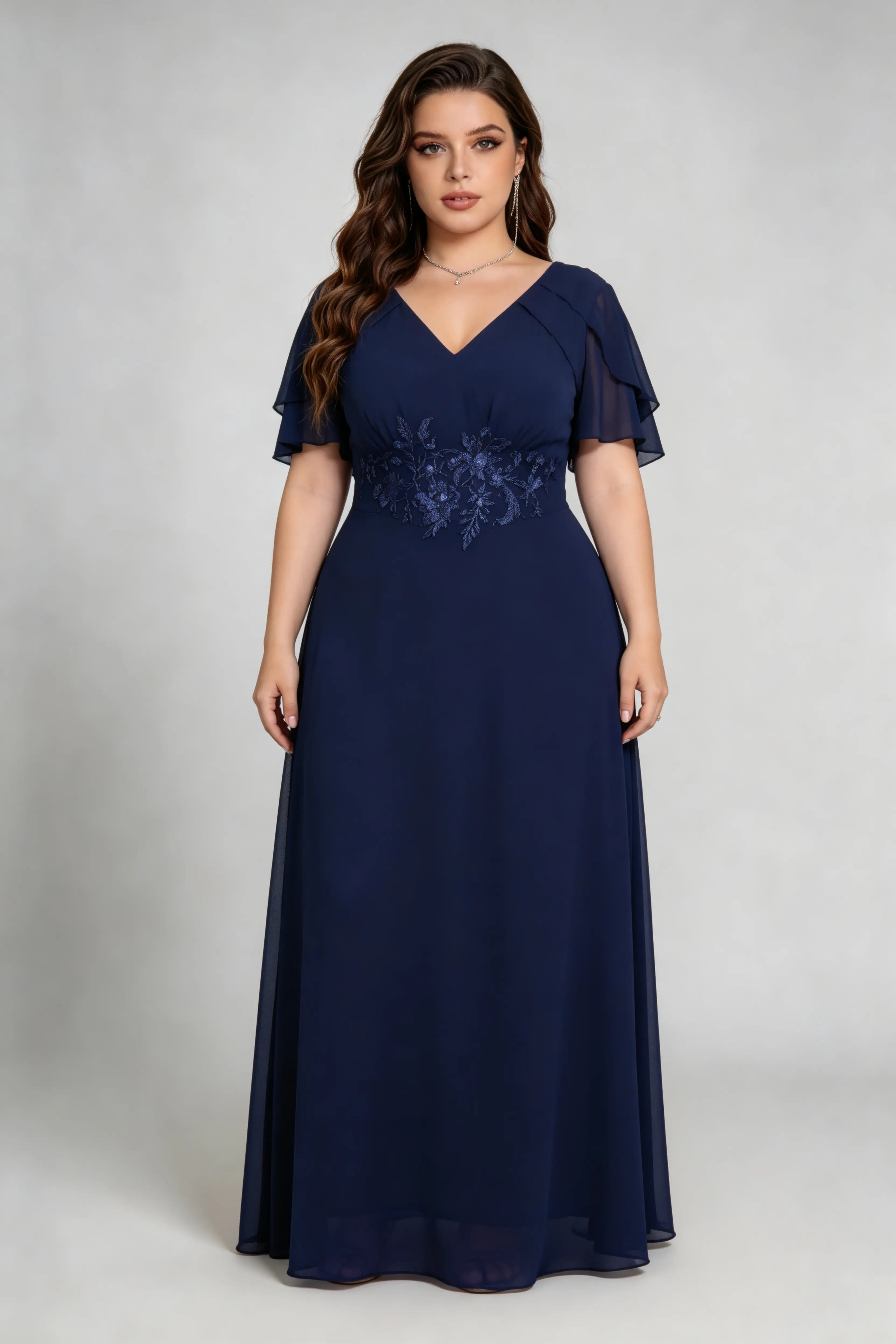 Plus size woman wearing navy floral embroidered chiffon maxi dress with ruffled sleeves, full length view