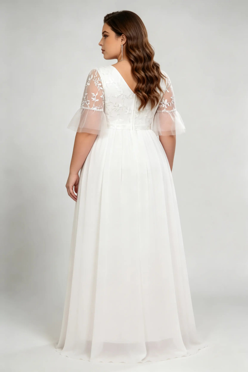 Curvy model wearing plus size white v-neck embroidered chiffon maxi wedding dress with flutter sleeves