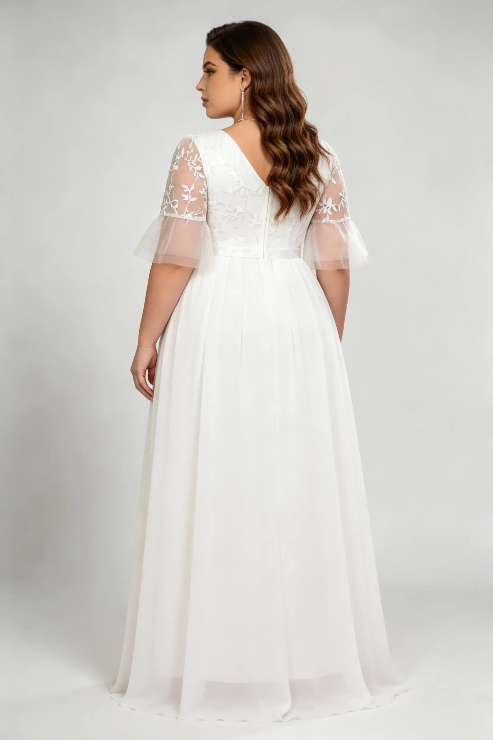 Curvy model wearing plus size white v-neck embroidered chiffon maxi wedding dress with flutter sleeves