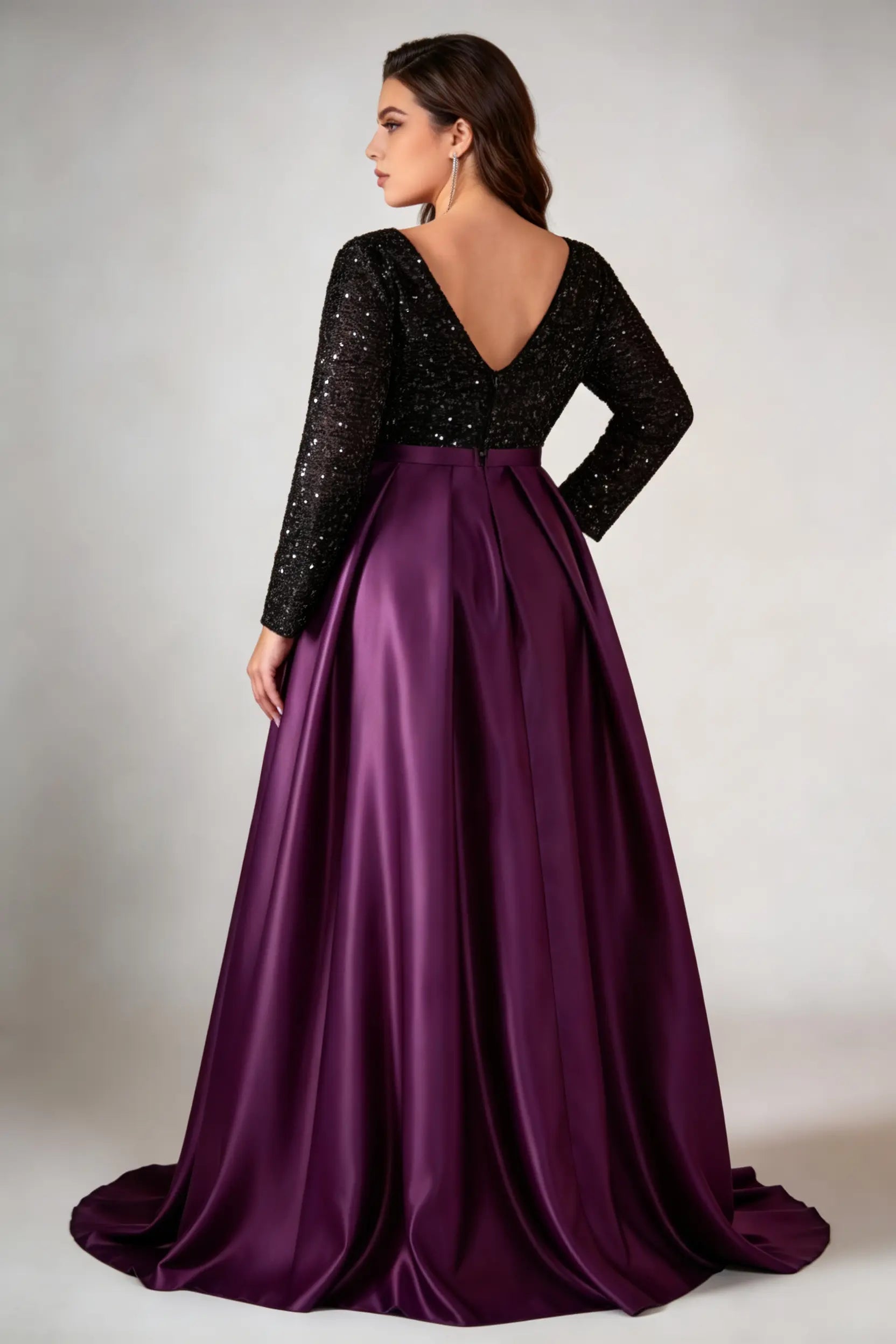 Curvy model wearing plus size black sequin v-neck long sleeve evening gown with high-slit satin skirt