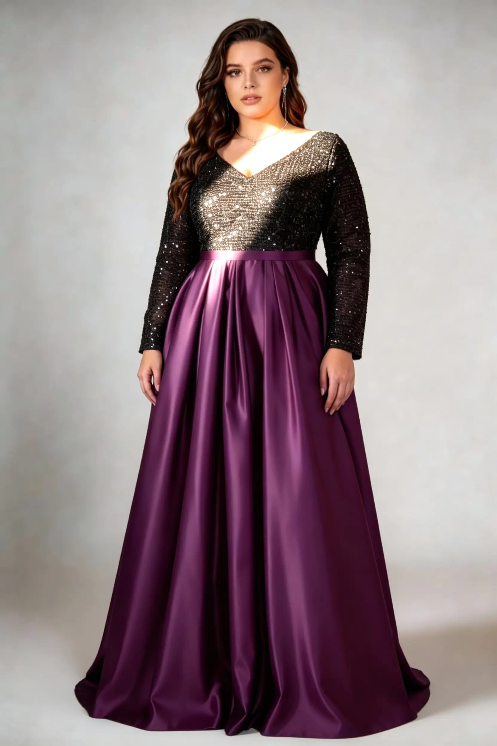 Curvy model wearing plus size black sequin v-neck long sleeve evening gown with high-slit satin skirt