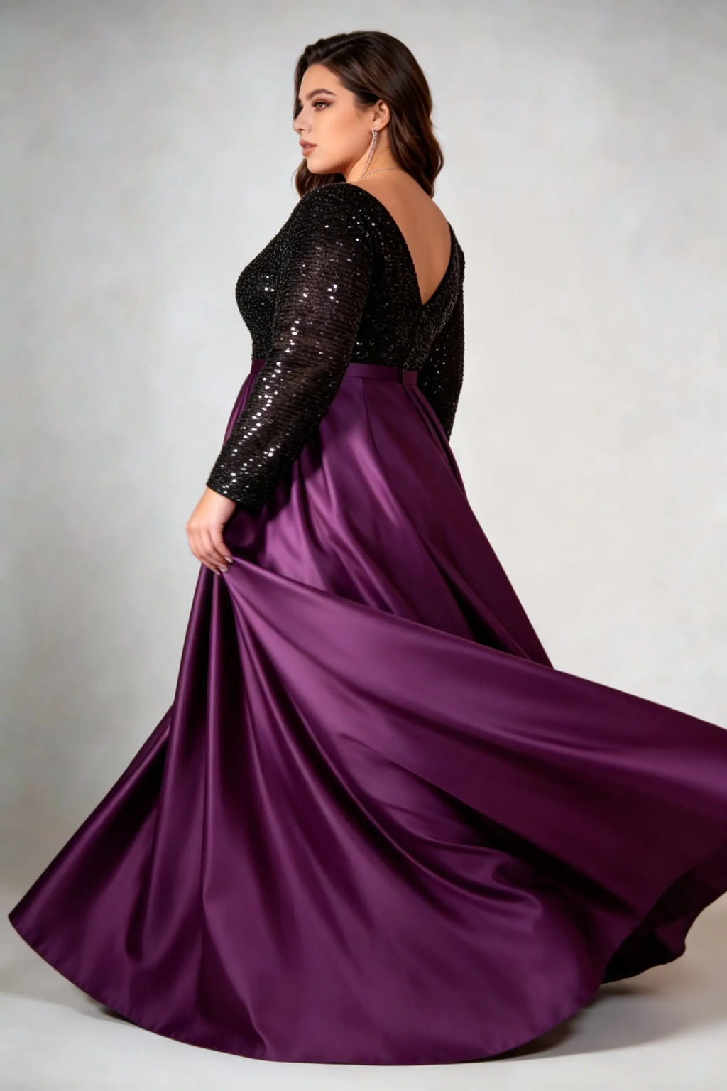 Curvy model wearing plus size black sequin v-neck long sleeve evening gown with high-slit satin skirt