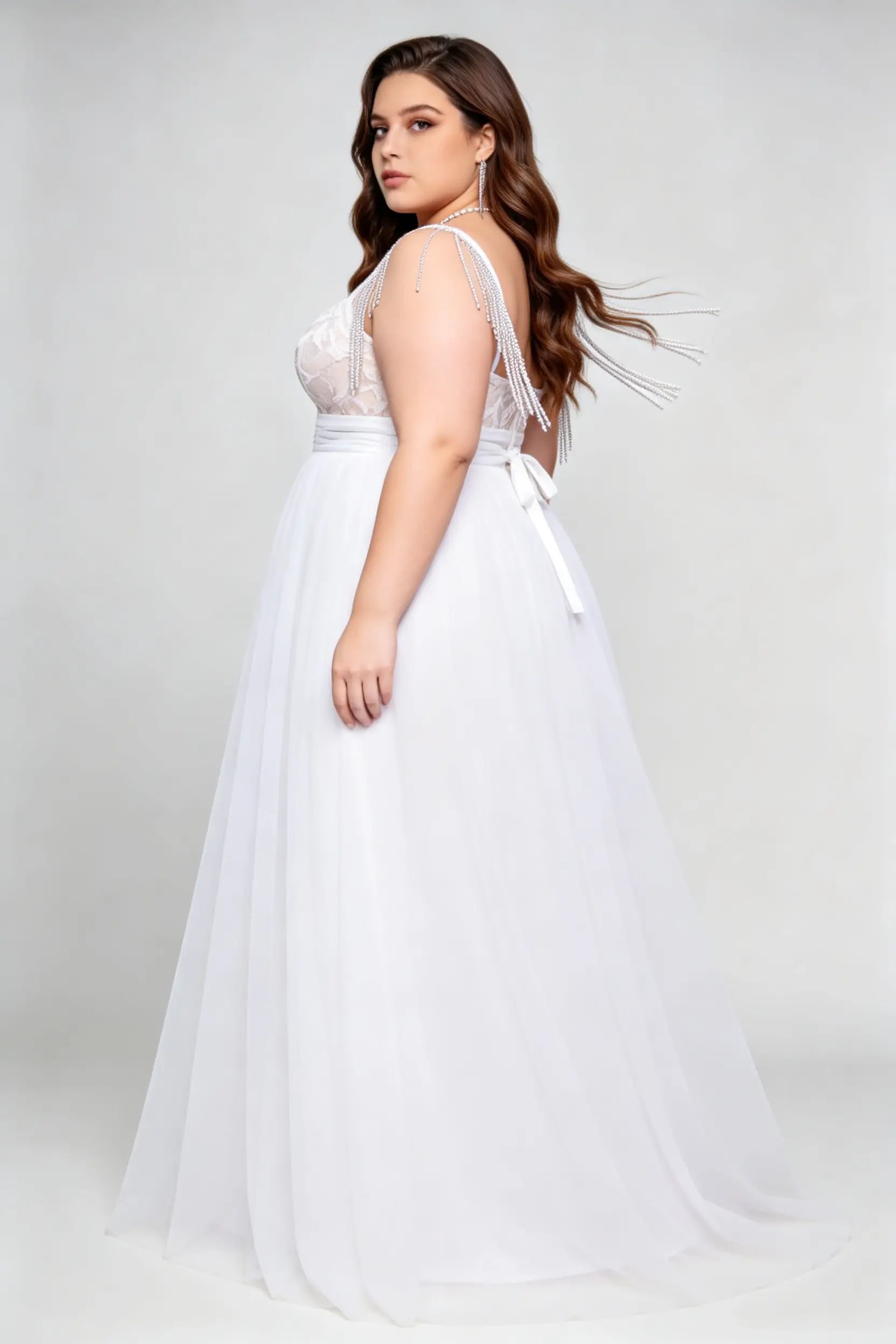 Curvy model wearing plus size white v-neck tulle bridal gown with rhinestone fringe shoulder straps