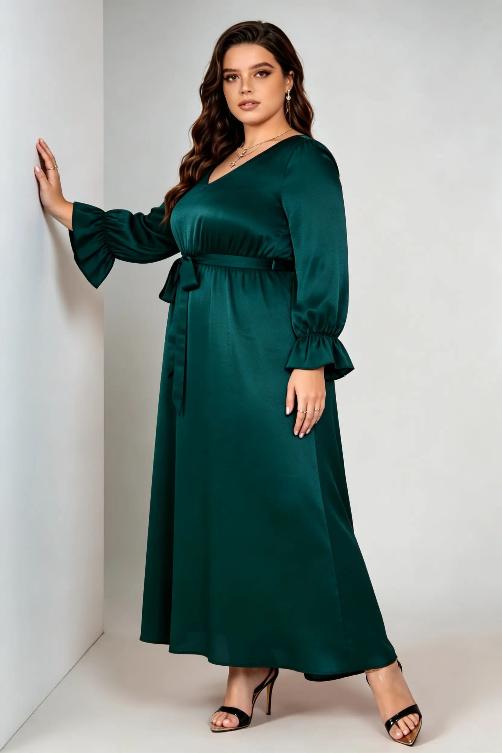 Curvy model wearing plus size dark green satin maxi dress, v-neck long sleeve ruffle cuff belted a-line elegant evening dress