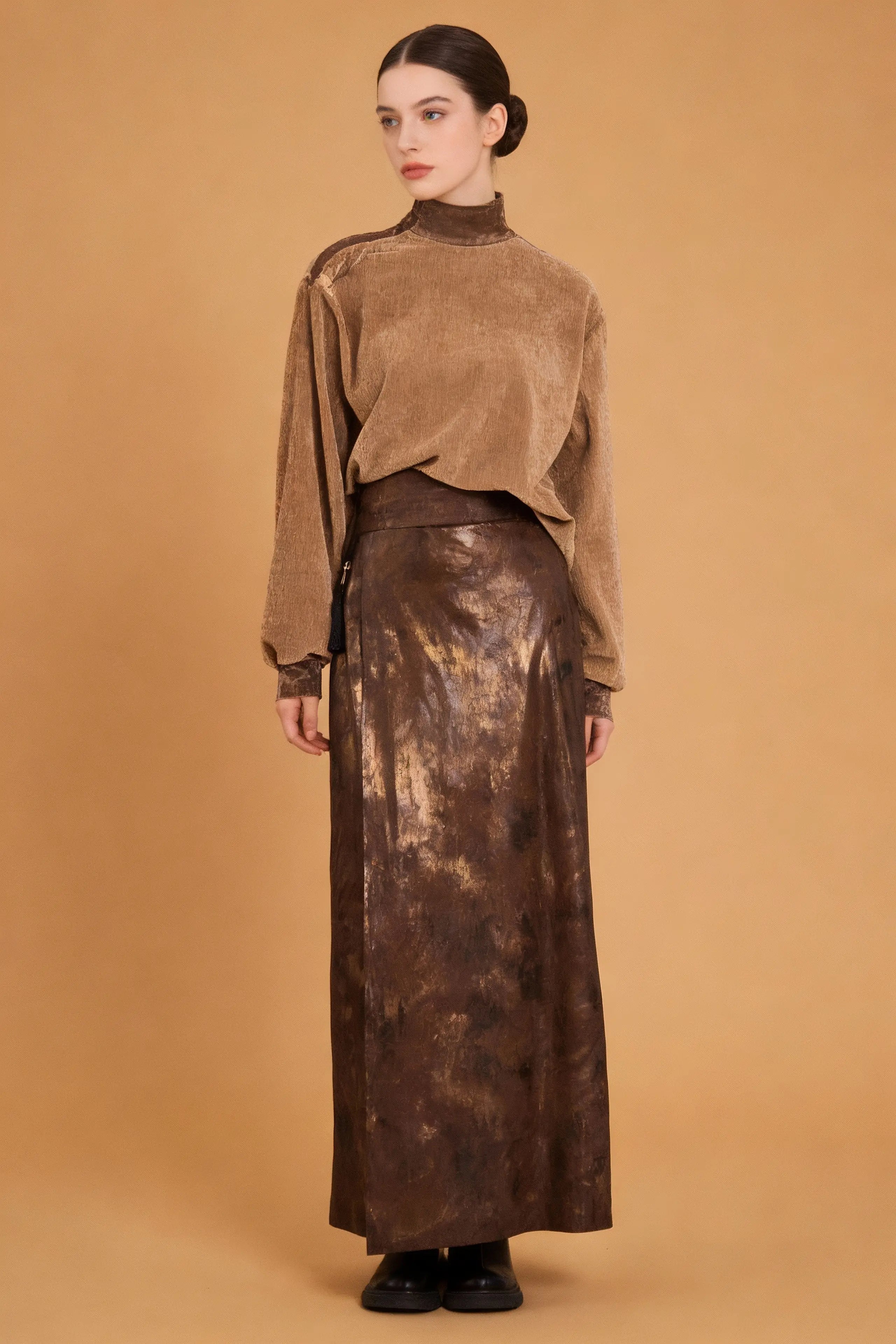 Woman wearing a brown velvet top and metallic skirt against a beige background