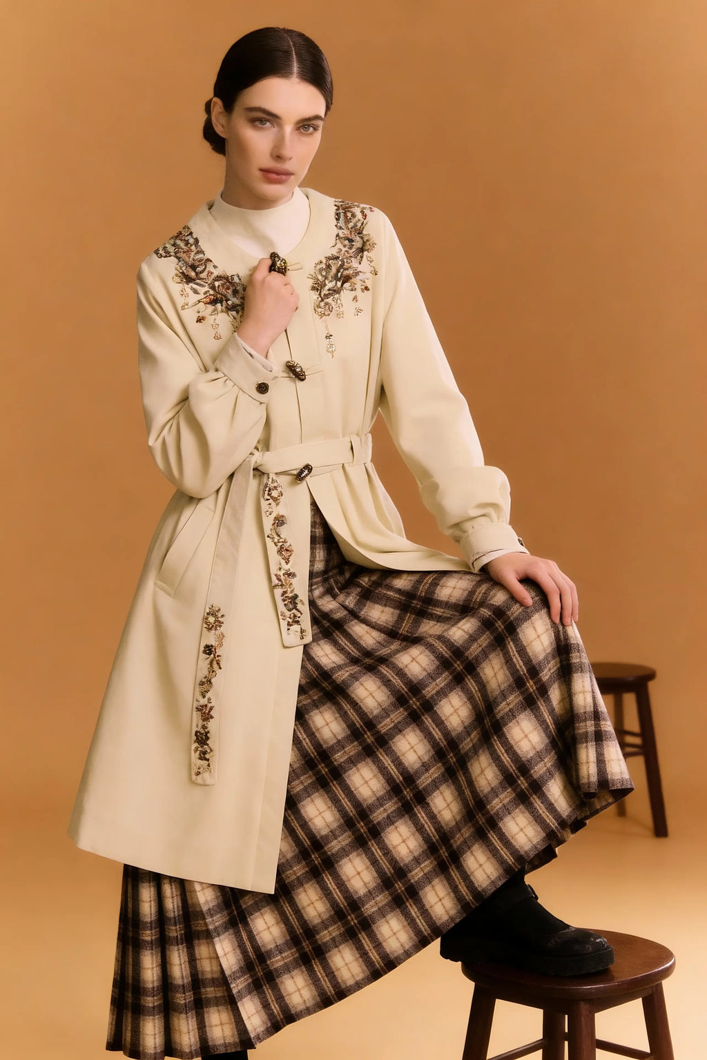 Woman wearing a long beige coat with floral embroidery on a brown background