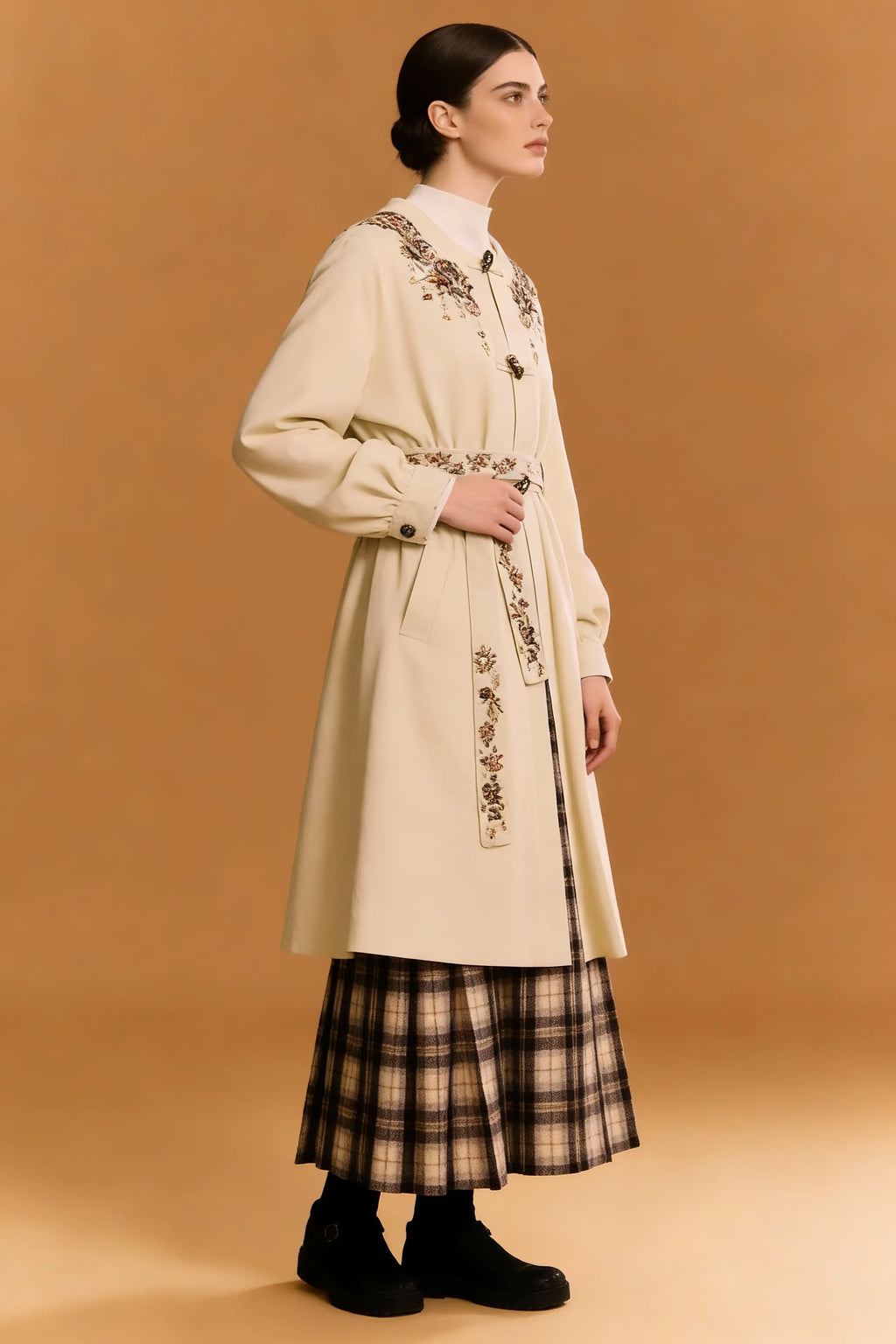 Woman wearing a long beige coat with floral embroidery on a brown background