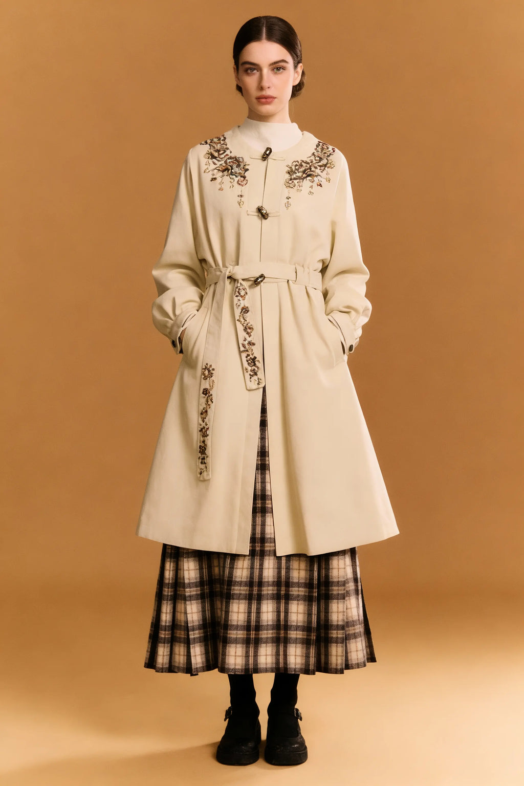 Woman wearing a long beige coat with floral embroidery on a brown background