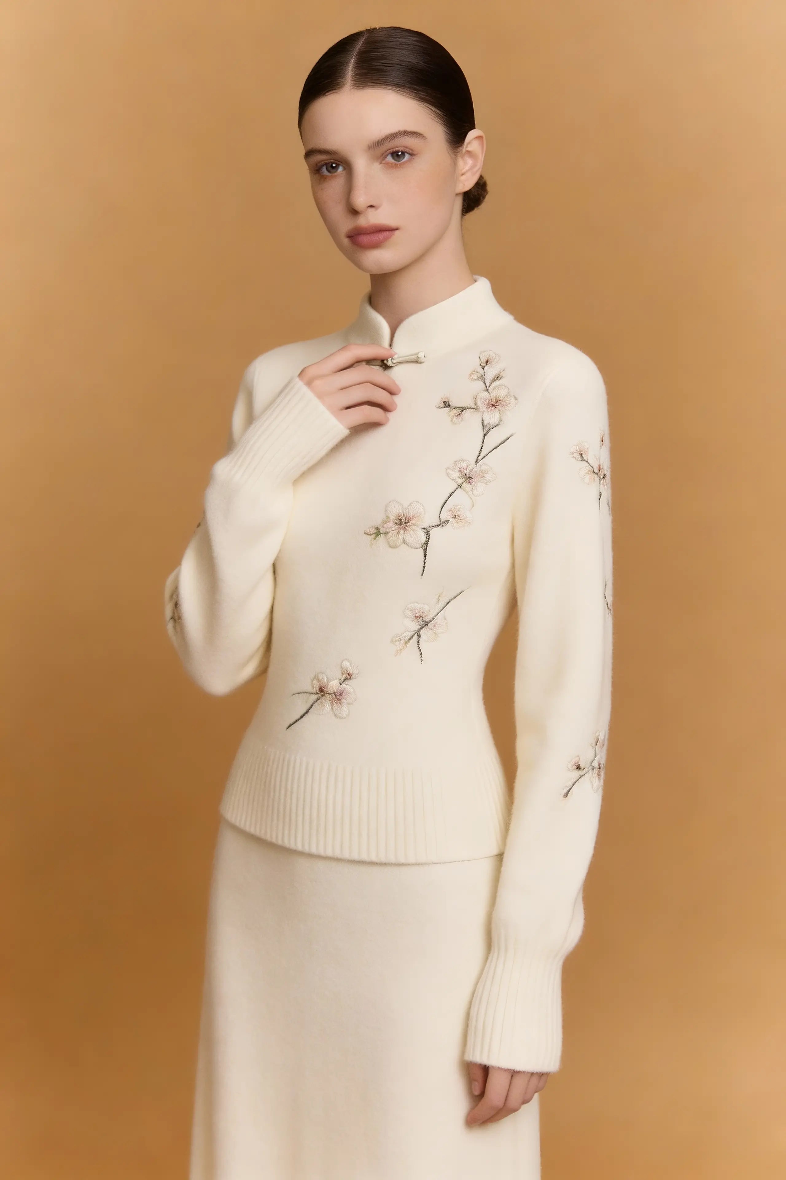 Woman wearing a cream-colored sweater with floral embroidery against a beige background