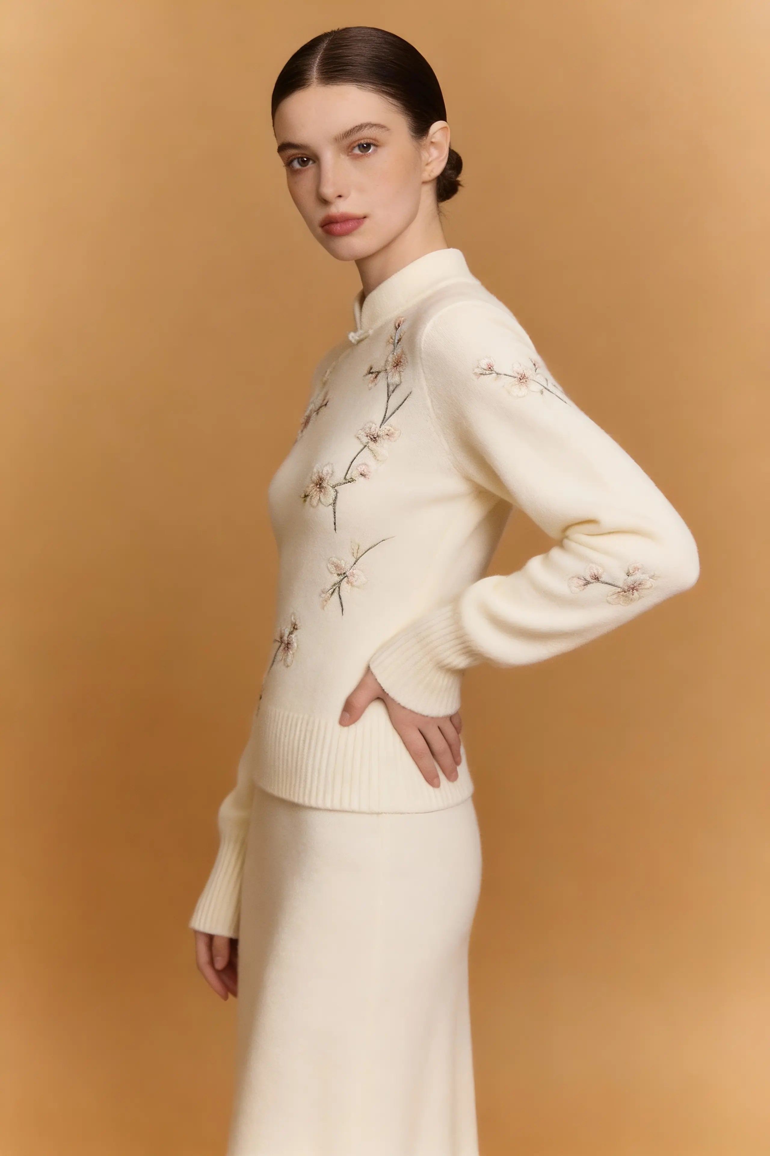 Woman wearing a cream-colored sweater with floral embroidery against a beige background
