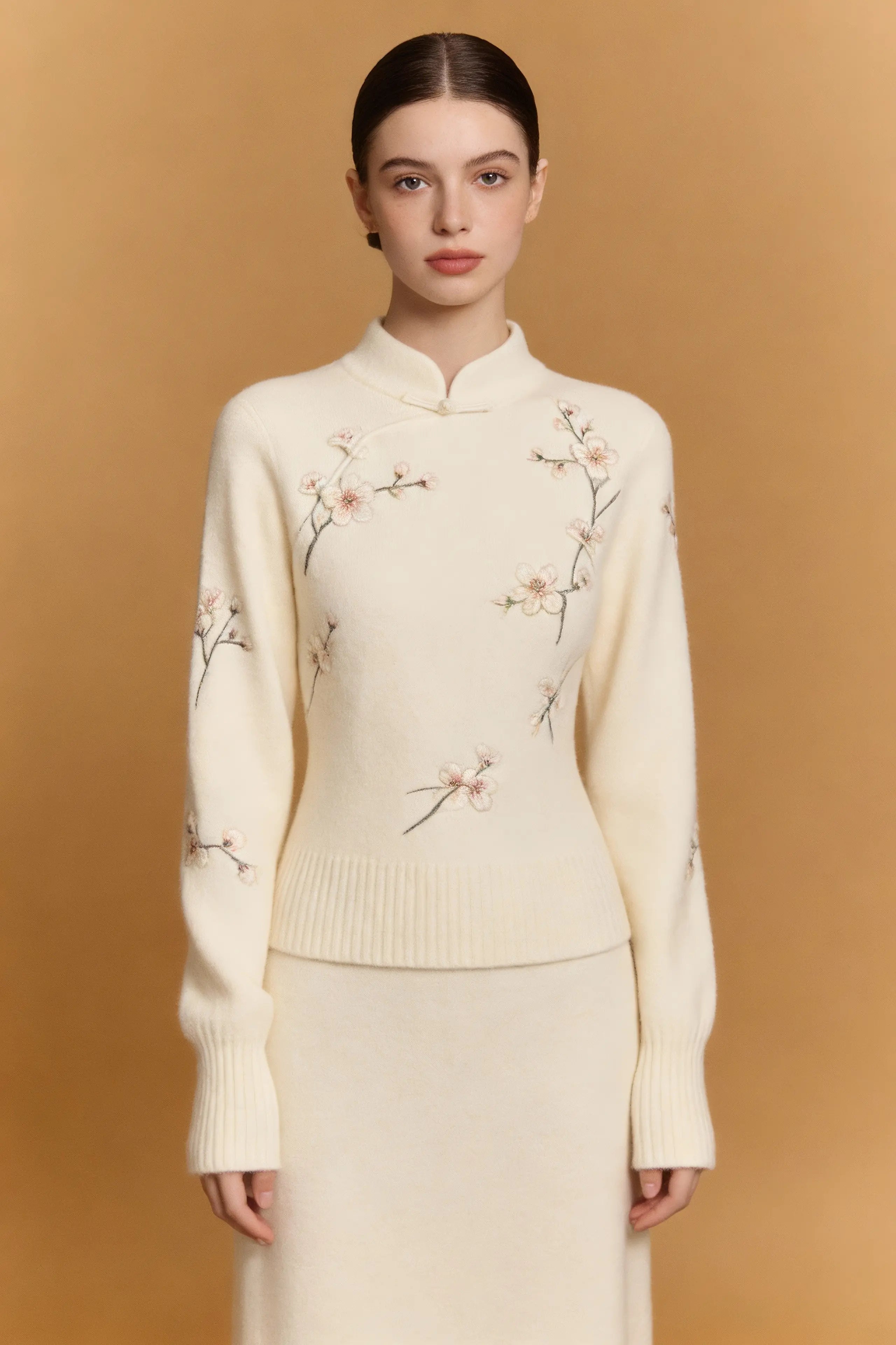 Woman wearing a cream-colored sweater with floral embroidery against a beige background
