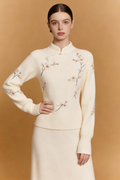Woman wearing a cream-colored sweater with floral embroidery against a beige background