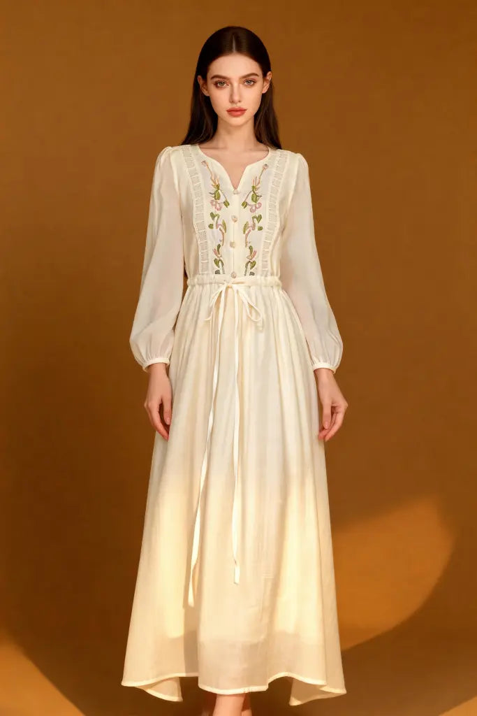 Woman wearing a Romantic Embroidered V-Neck Maxi Dress - White Boho Chic Long Sleeve Evening Gown on a brown background