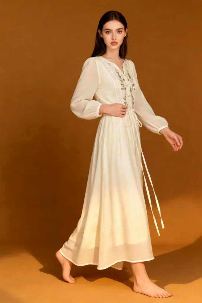 Woman wearing a Romantic Embroidered V-Neck Maxi Dress - White Boho Chic Long Sleeve Evening Gown on a brown background