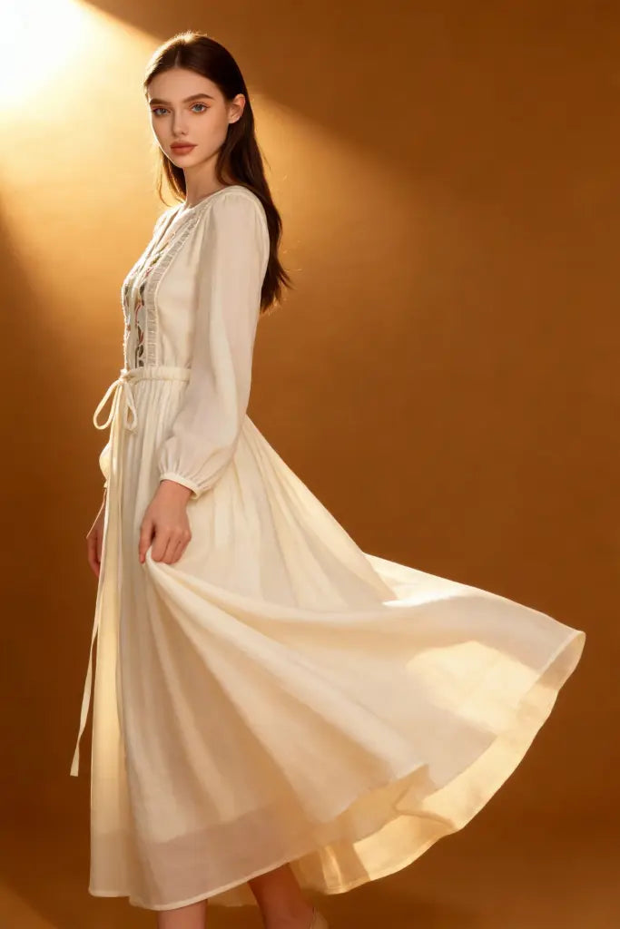 Woman wearing a Romantic Embroidered V-Neck Maxi Dress - White Boho Chic Long Sleeve Evening Gown on a brown background