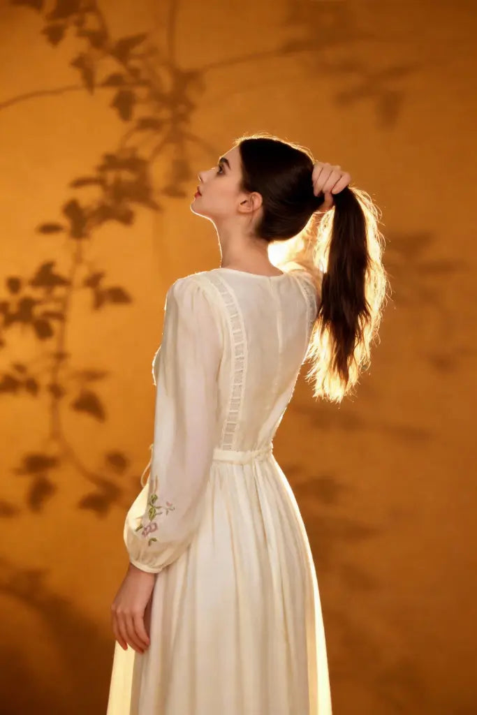 Woman wearing a Romantic Embroidered V-Neck Maxi Dress - White Boho Chic Long Sleeve Evening Gown on a brown background