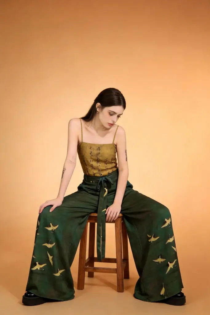 Woman sitting on a stool wearing a green outfit with bird patterns against an orange background