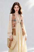 Woman wearing a Bohemian Egyptian Print Fringed Vest with Flowy Beige Maxi Dress and holding a straw bag on a light gray background