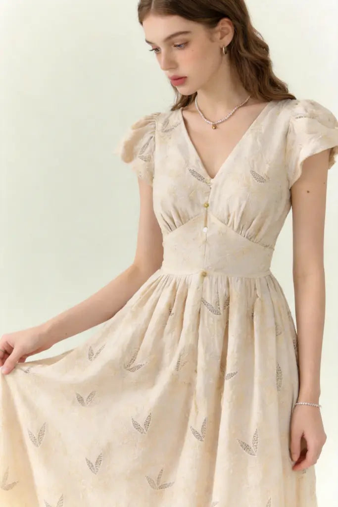 Woman wearing a beige dress with vintage embroidered linen-blend midi dress with ruffled cap sleeves on a white background