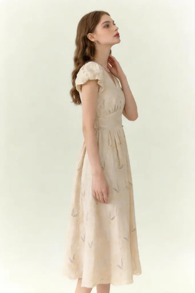Woman wearing a beige dress with vintage embroidered linen-blend midi dress with ruffled cap sleeves on a white background