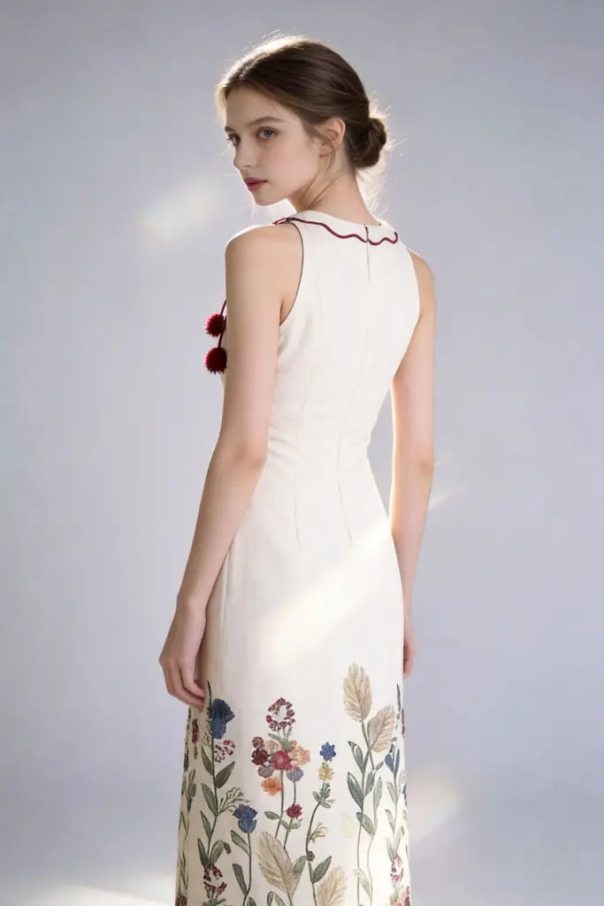 Woman wearing a elegant acrylic floral embroidered halter maxi white dress with tassel detail on a plain background