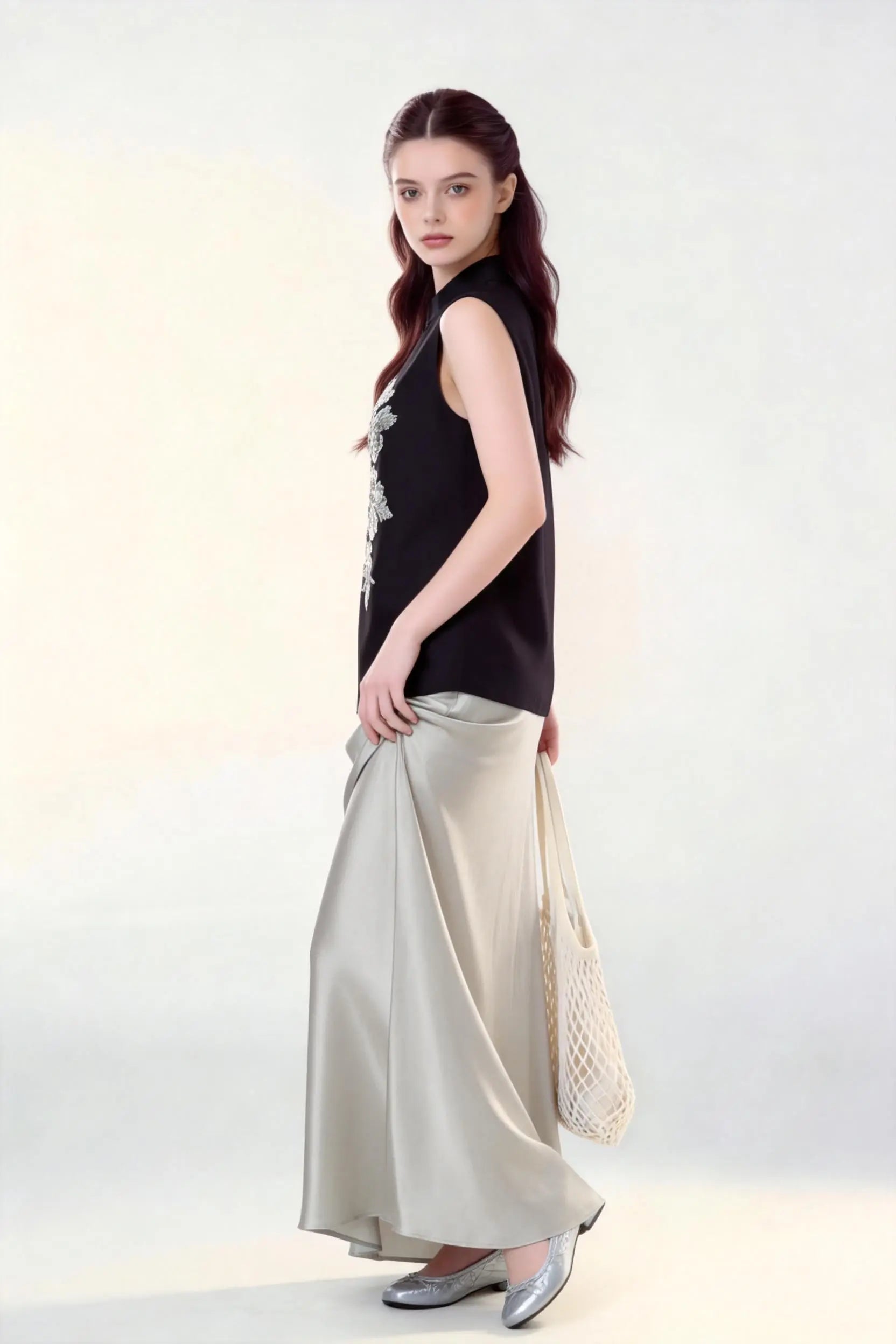 Woman wearing a black Beaded Lotus Embroidery Loose Sleeveless Top & Satin Skirt Two-Piece Set, holding a woven bag on a white background.