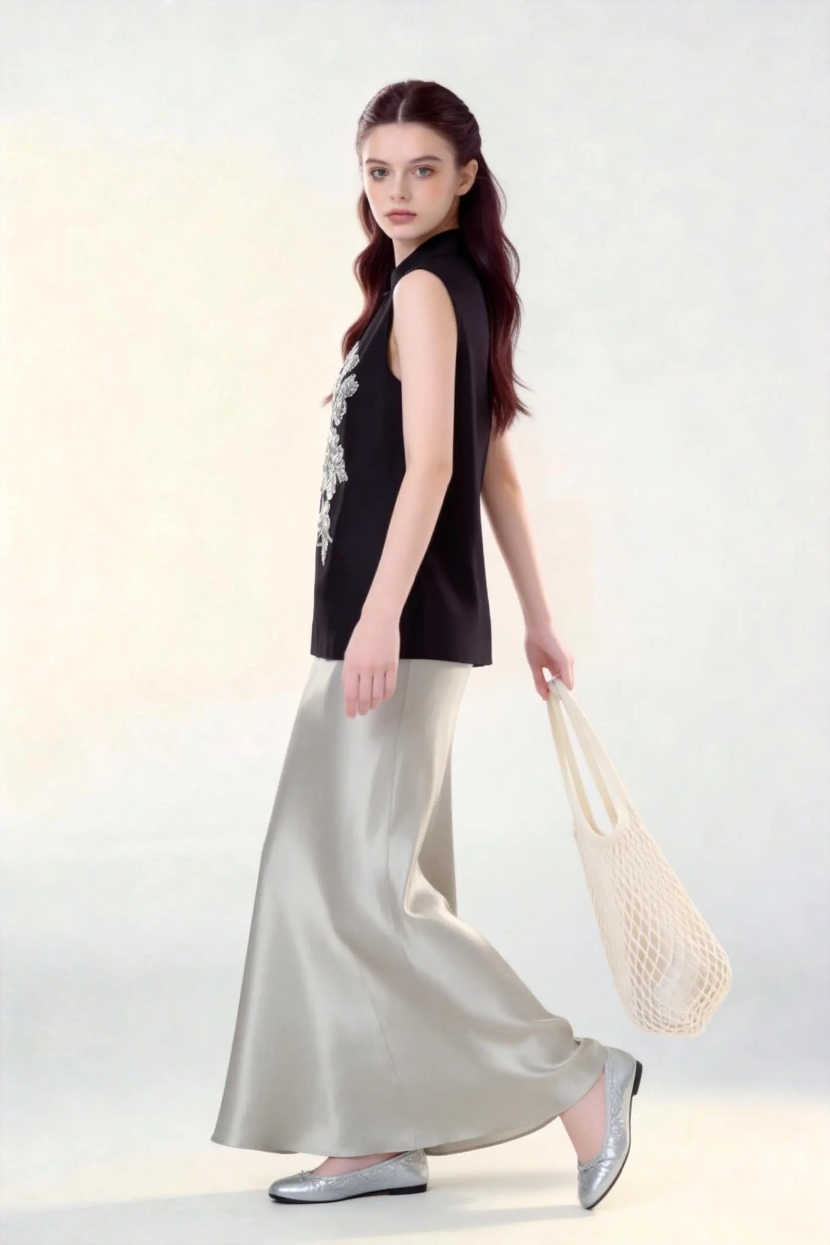 Woman wearing a black Beaded Lotus Embroidery Loose Sleeveless Top & Satin Skirt Two-Piece Set, holding a woven bag on a white background.