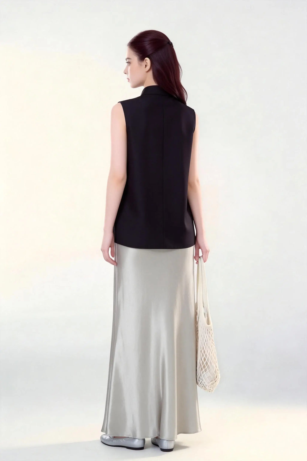 Woman wearing a black Beaded Lotus Embroidery Loose Sleeveless Top & Satin Skirt Two-Piece Set, holding a woven bag on a white background.