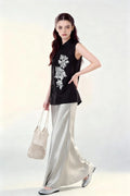Woman wearing a black Beaded Lotus Embroidery Loose Sleeveless Top & Satin Skirt Two-Piece Set, holding a woven bag on a white background.