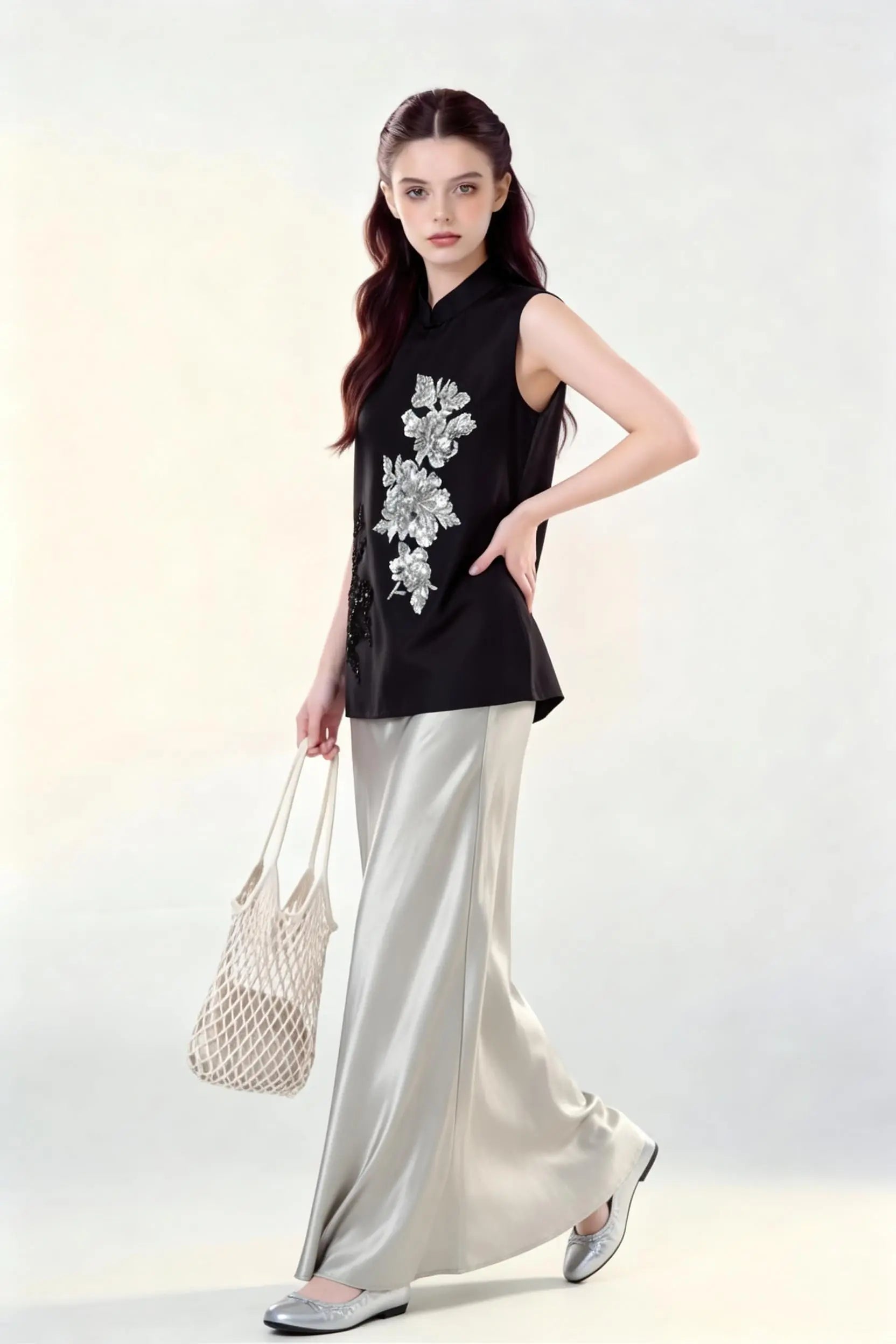 Woman wearing a black Beaded Lotus Embroidery Loose Sleeveless Top & Satin Skirt Two-Piece Set, holding a woven bag on a white background.