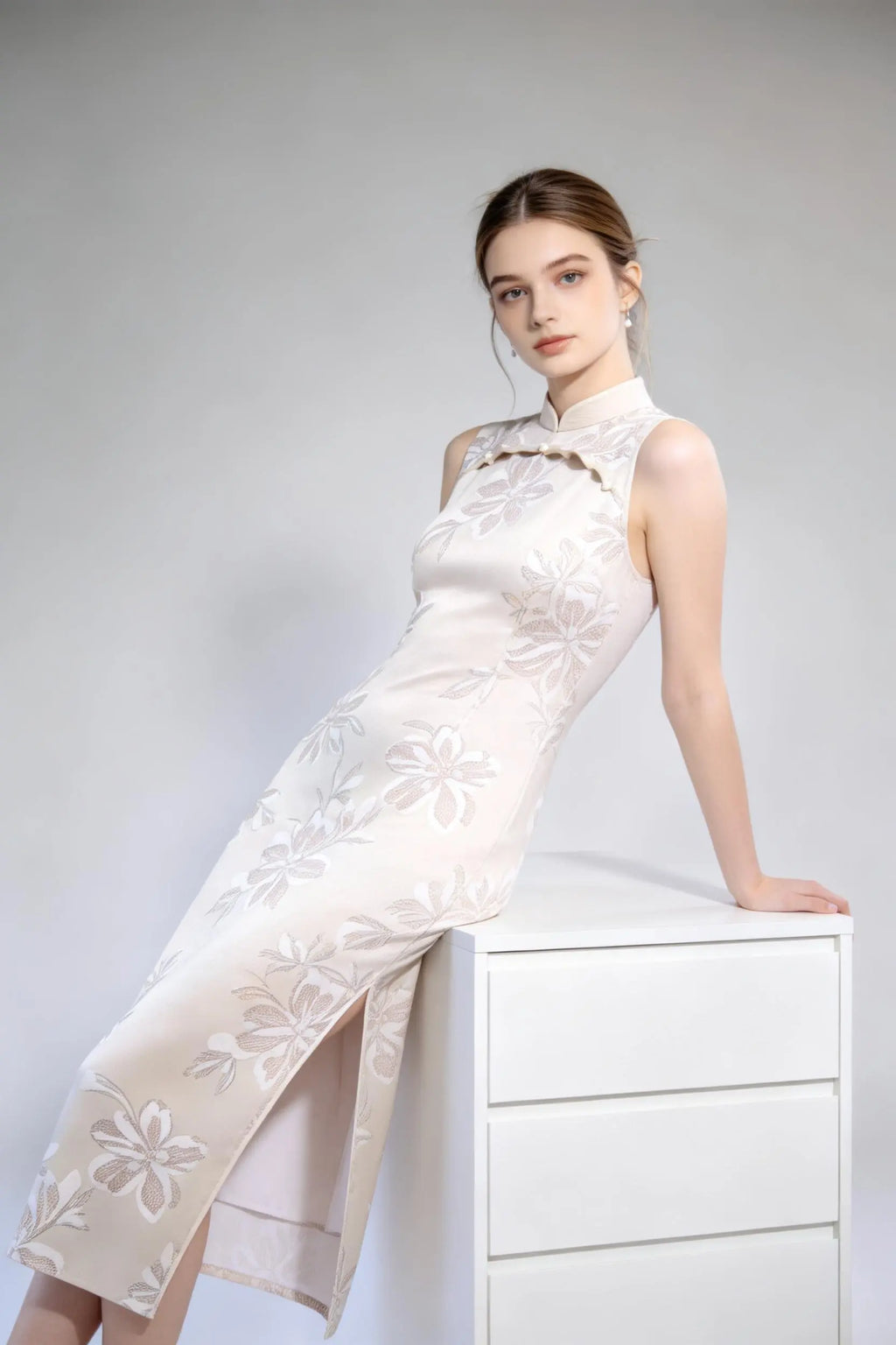 Woman wearing sleeveless floral embroidery cheongsam with cutout frog buttons, double-lined mandarin collar qipao dress against a plain background