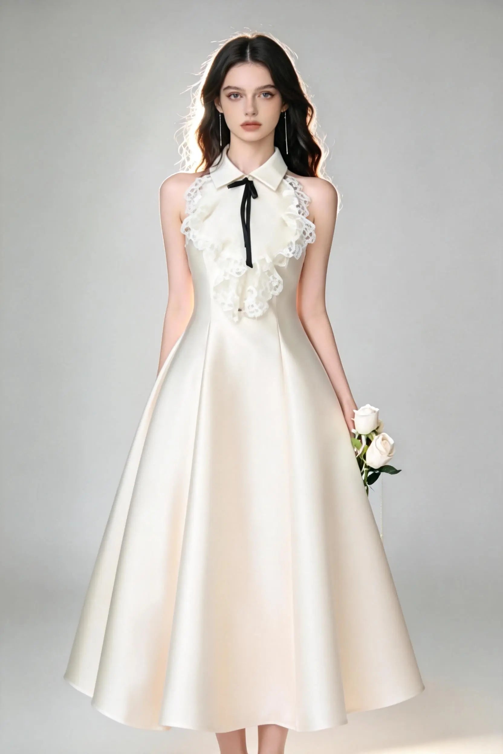 Woman in a white elegant halter neck satin flared a-line dress with lace collar and bow detail standing against a gray background