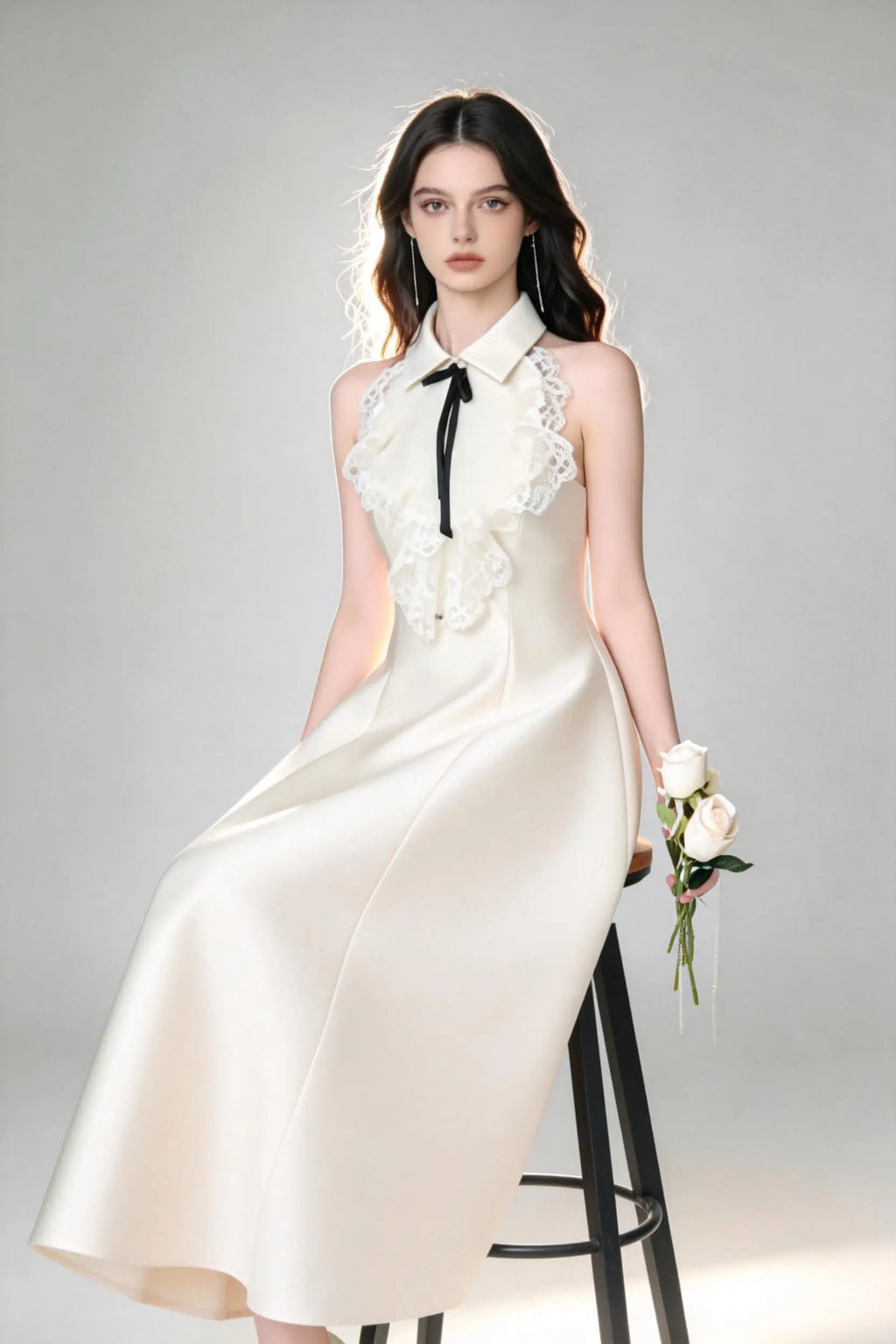 Woman in a white elegant halter neck satin flared a-line dress with lace collar and bow detail standing against a gray background