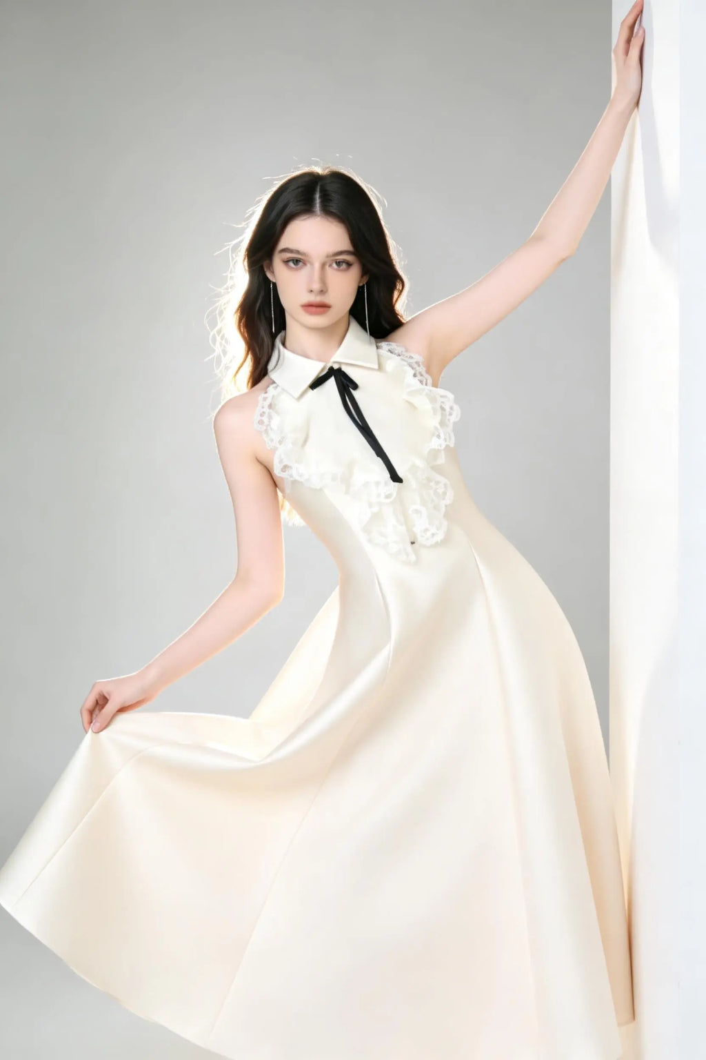 Woman in a white elegant halter neck satin flared a-line dress with lace collar and bow detail standing against a gray background