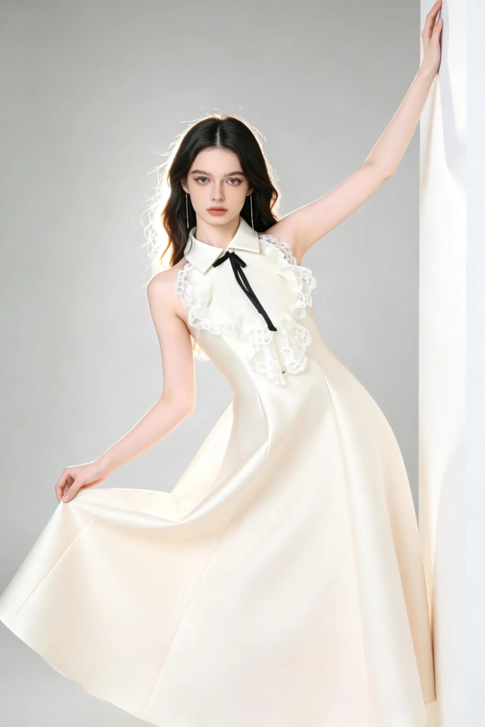 Woman in a white elegant halter neck satin flared a-line dress with lace collar and bow detail standing against a gray background