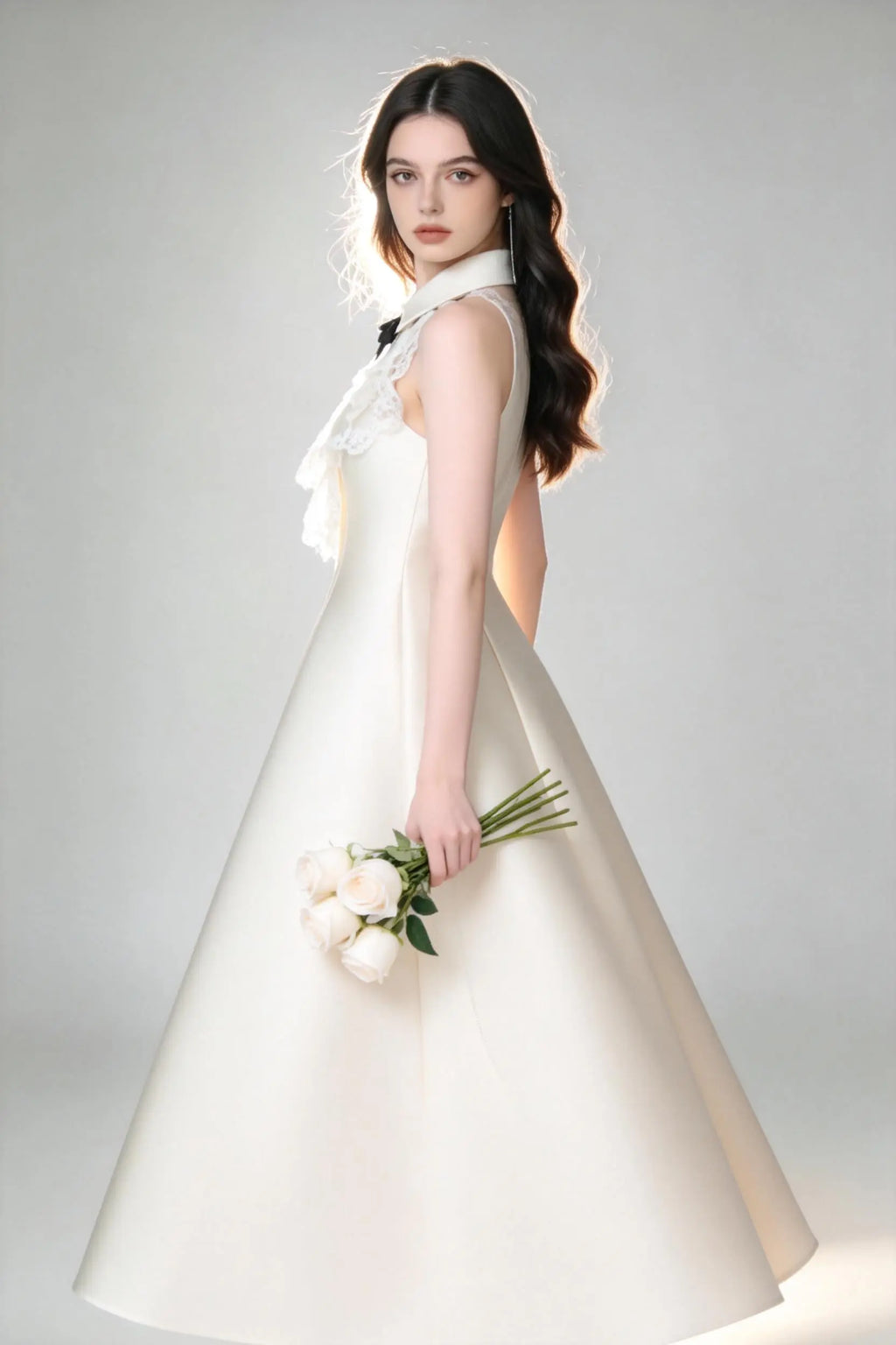 Woman in a white elegant halter neck satin flared a-line dress with lace collar and bow detail standing against a gray background