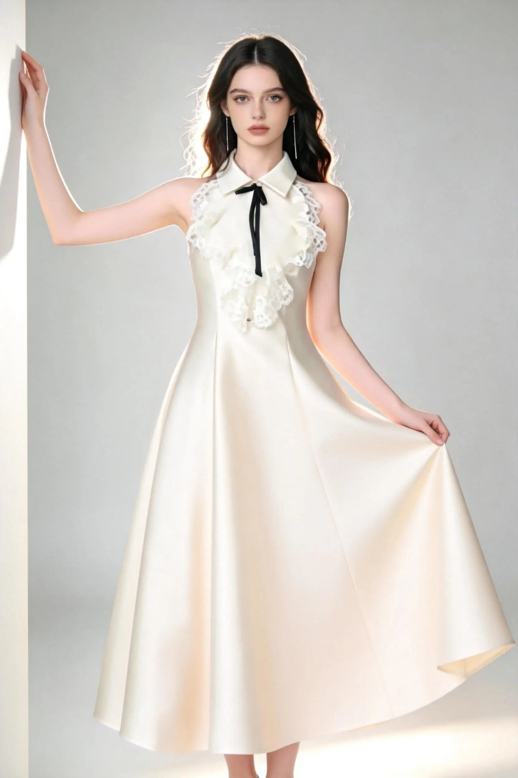 Woman in a white elegant halter neck satin flared a-line dress with lace collar and bow detail standing against a gray background