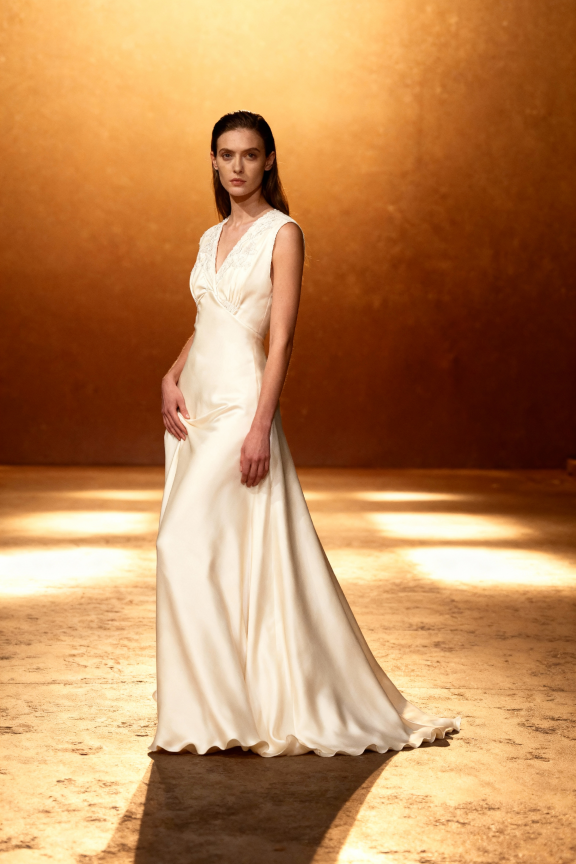 Woman in a white dress standing against a warm-toned wall.