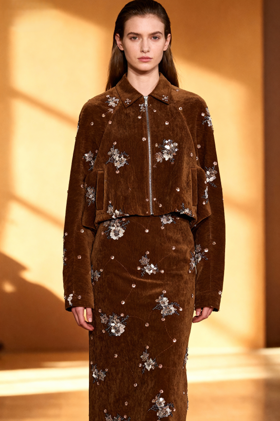 Woman wearing a brown velvet outfit with floral embellishments on a warm-toned background
