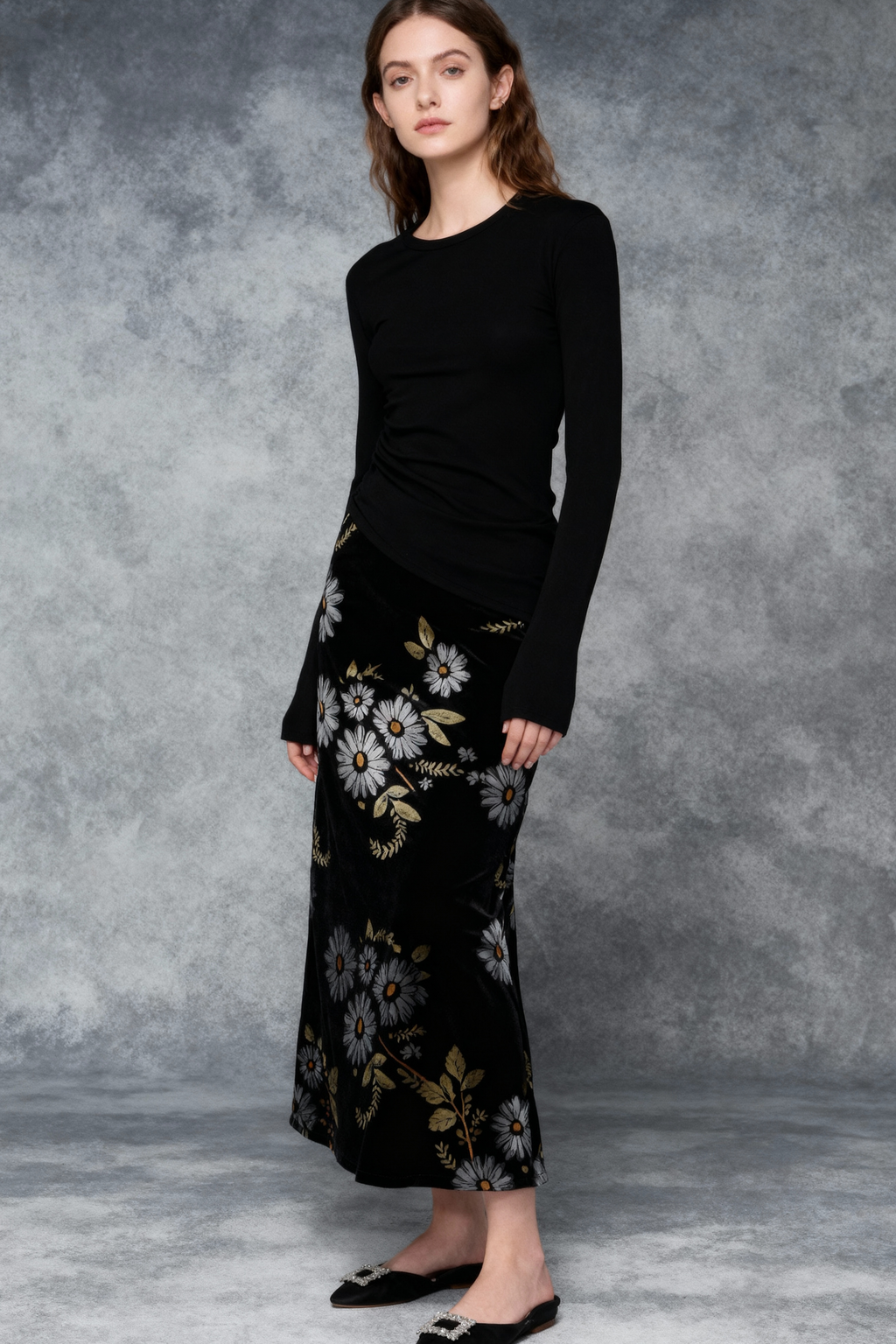 Woman wearing a black long-sleeve top and floral skirt against a gray background