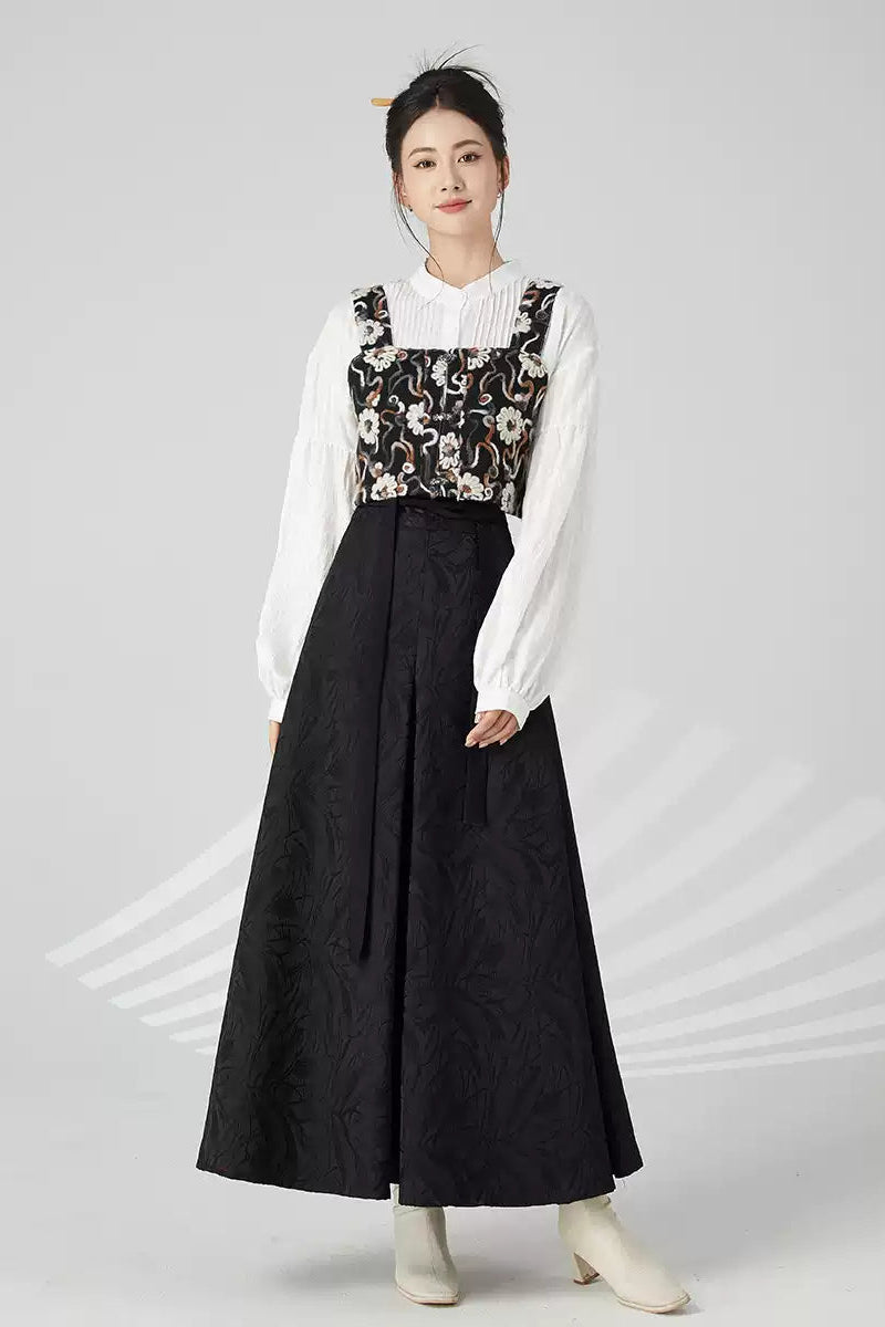 Woman wearing a white blouse with floral vest and black skirt on a gray background