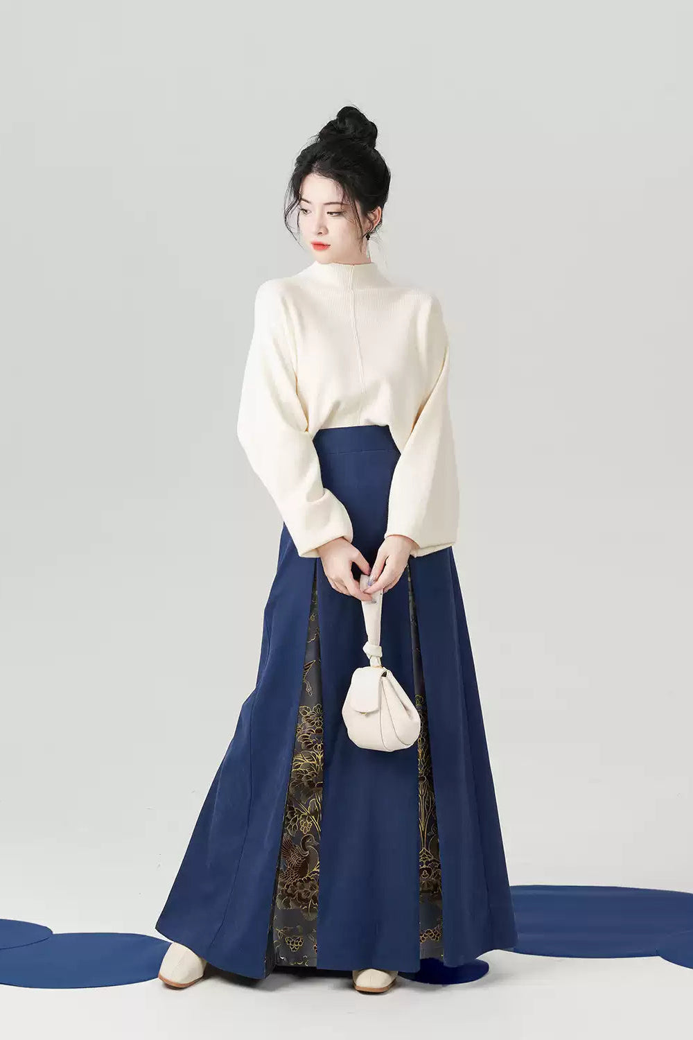 Woman wearing a white top and blue skirt holding a white bag on a gray background