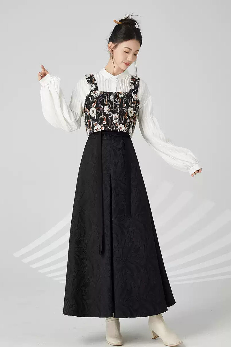 Woman wearing a white blouse with floral vest and black skirt on a gray background