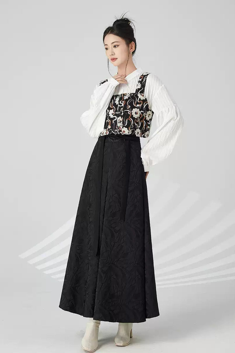 Woman wearing a white blouse with floral vest and black skirt on a gray background