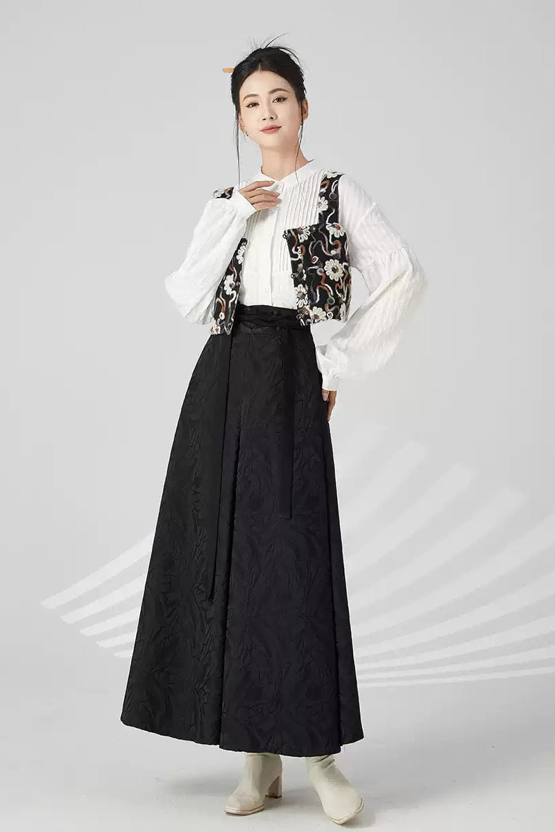 Woman wearing a white blouse with floral vest and black skirt on a gray background